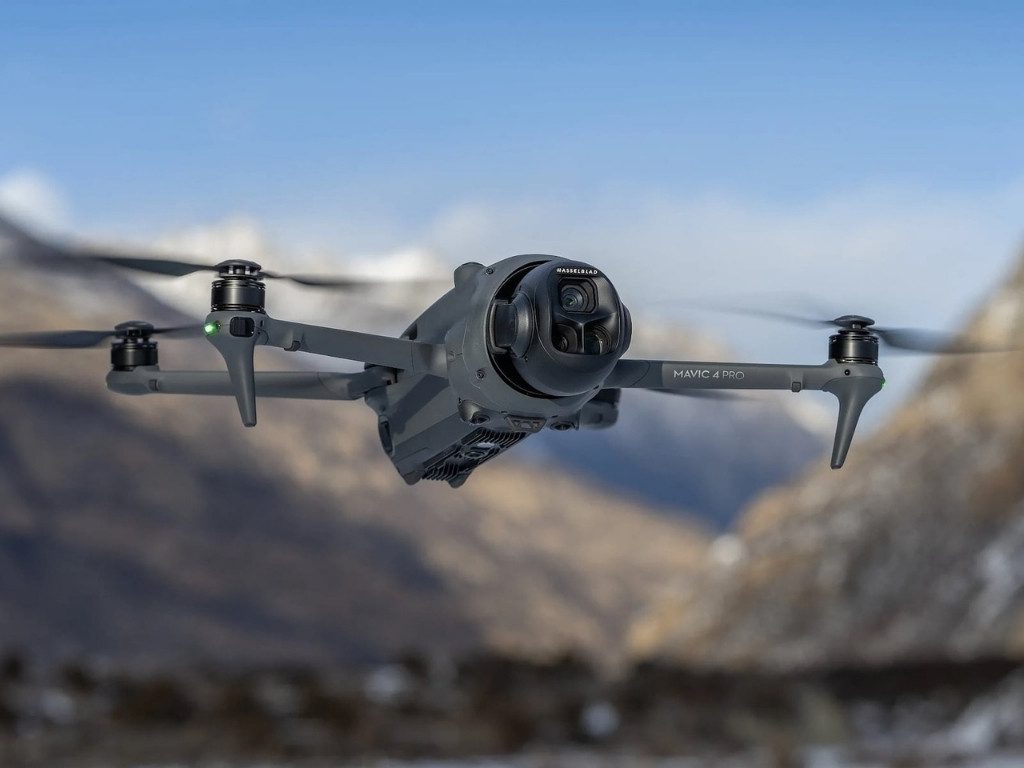 Drone DJI Mavic 4 Pro en vol devant un paysage de montagnes enneigées.